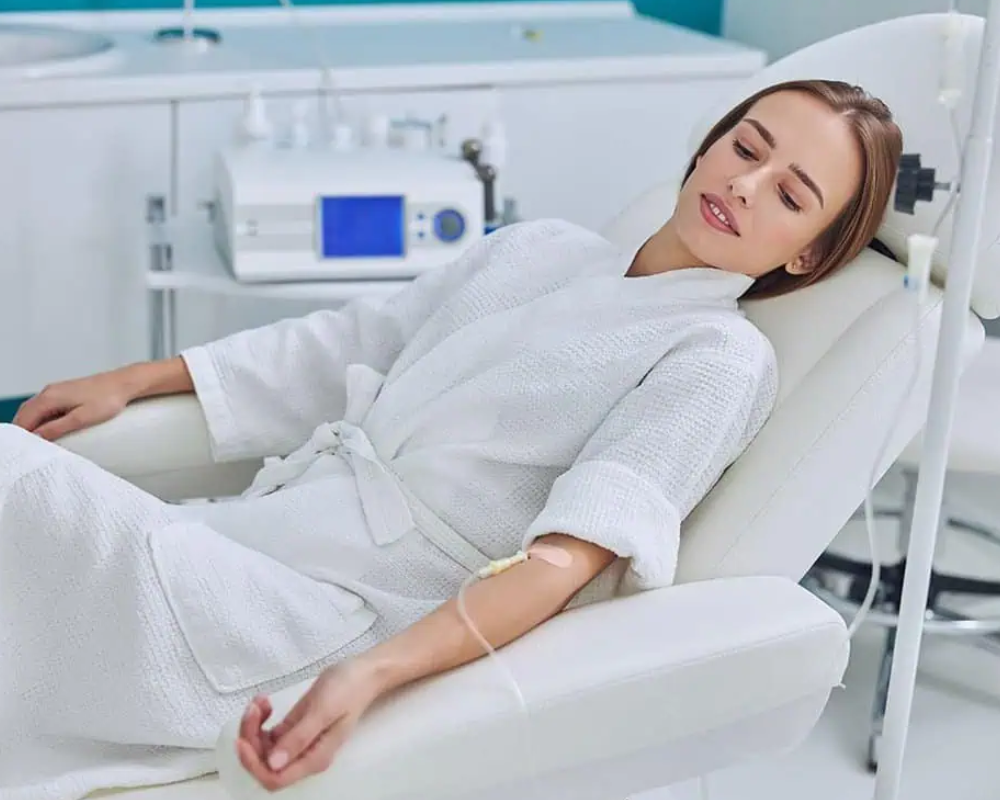 Mujer en bata recibiendo tratamiento intravenoso.