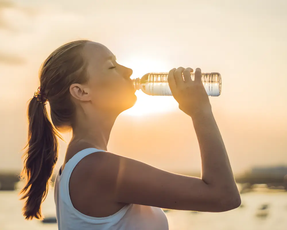 Mujer bebiendo agua al atardecer